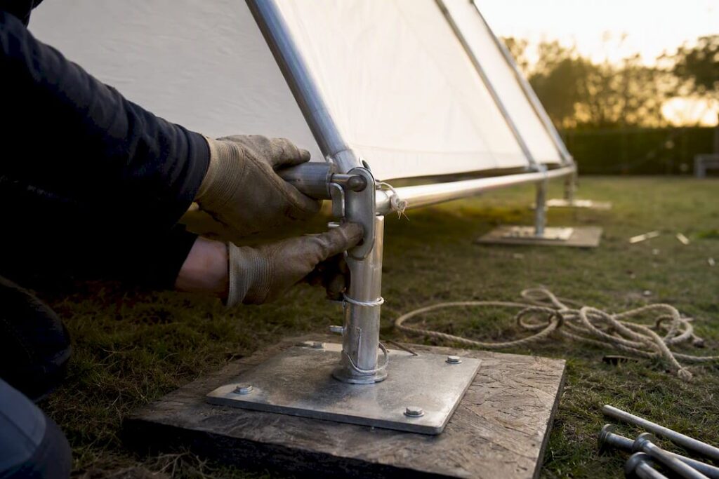 Mani che montano la struttura di una tenda su un prato in pendenza